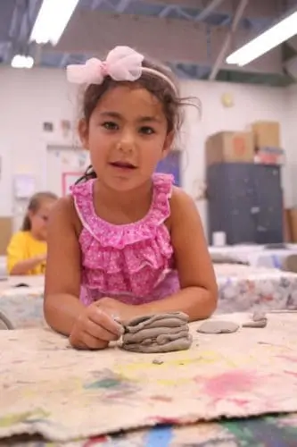 A young girl enjoys making a coil pot in The Art League's Art Camp.